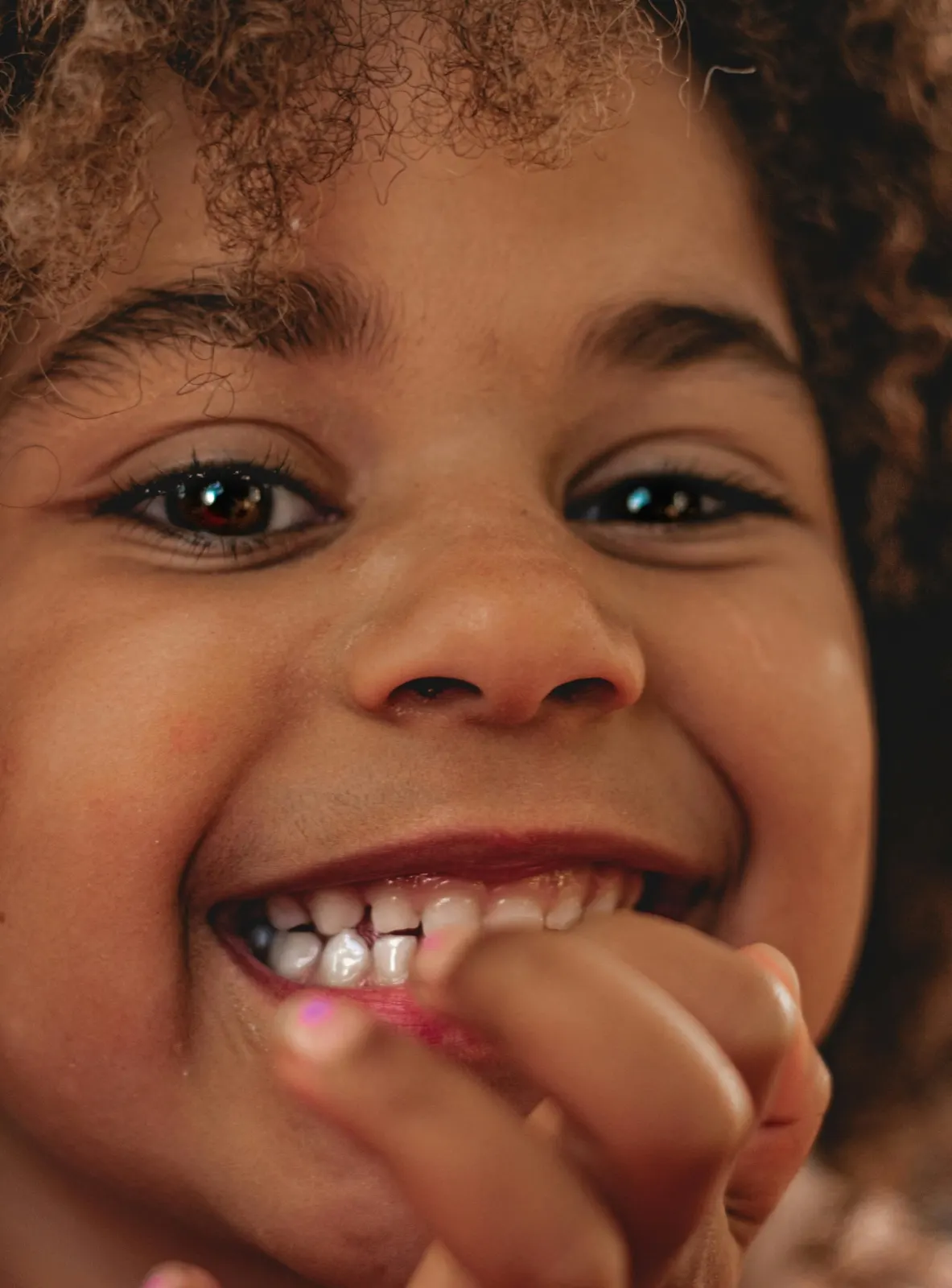 Smiling child with a hand near their mouth